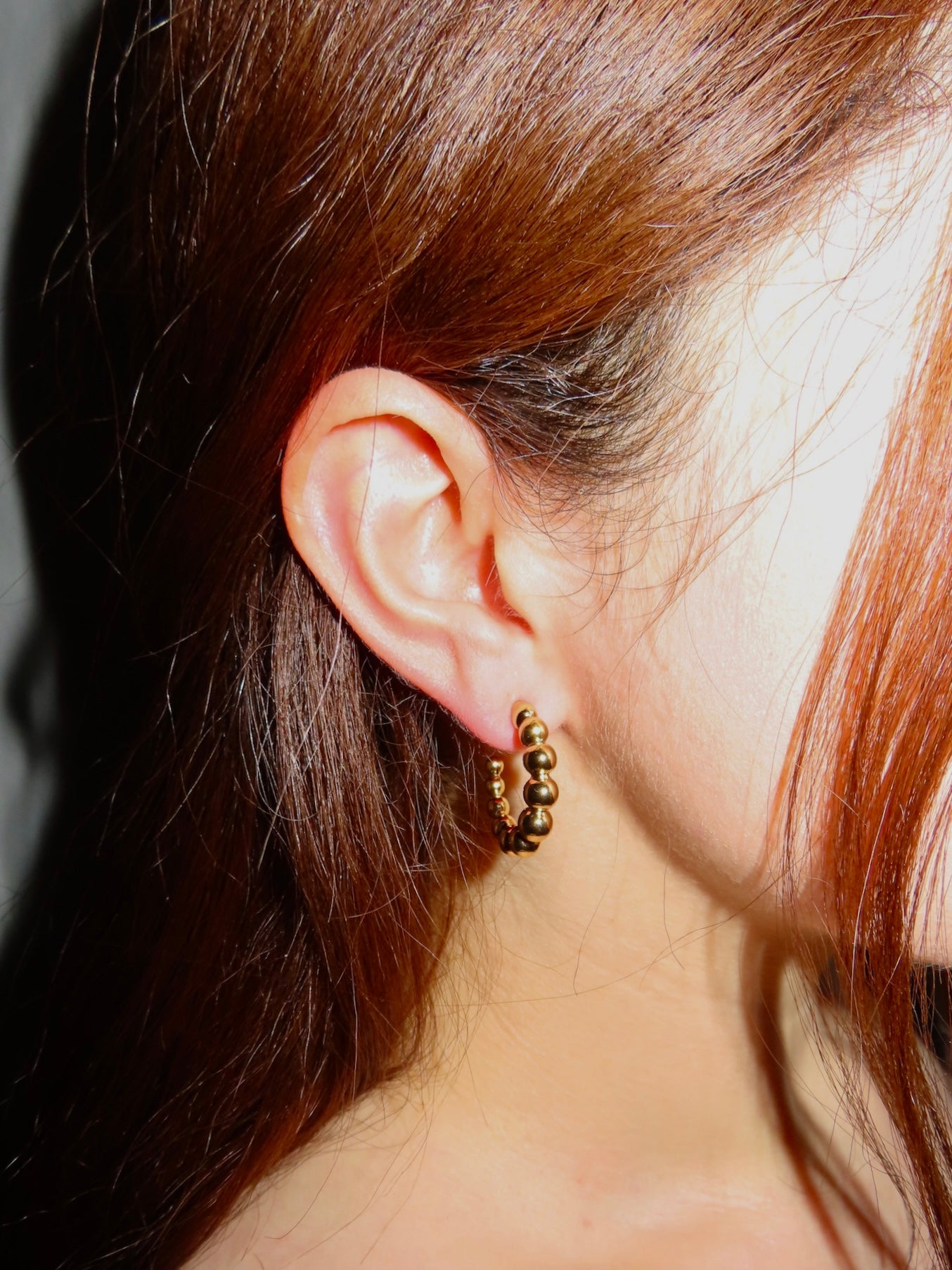 Close-up of an ear wearing a gold earring with hair partially obscuring the view.